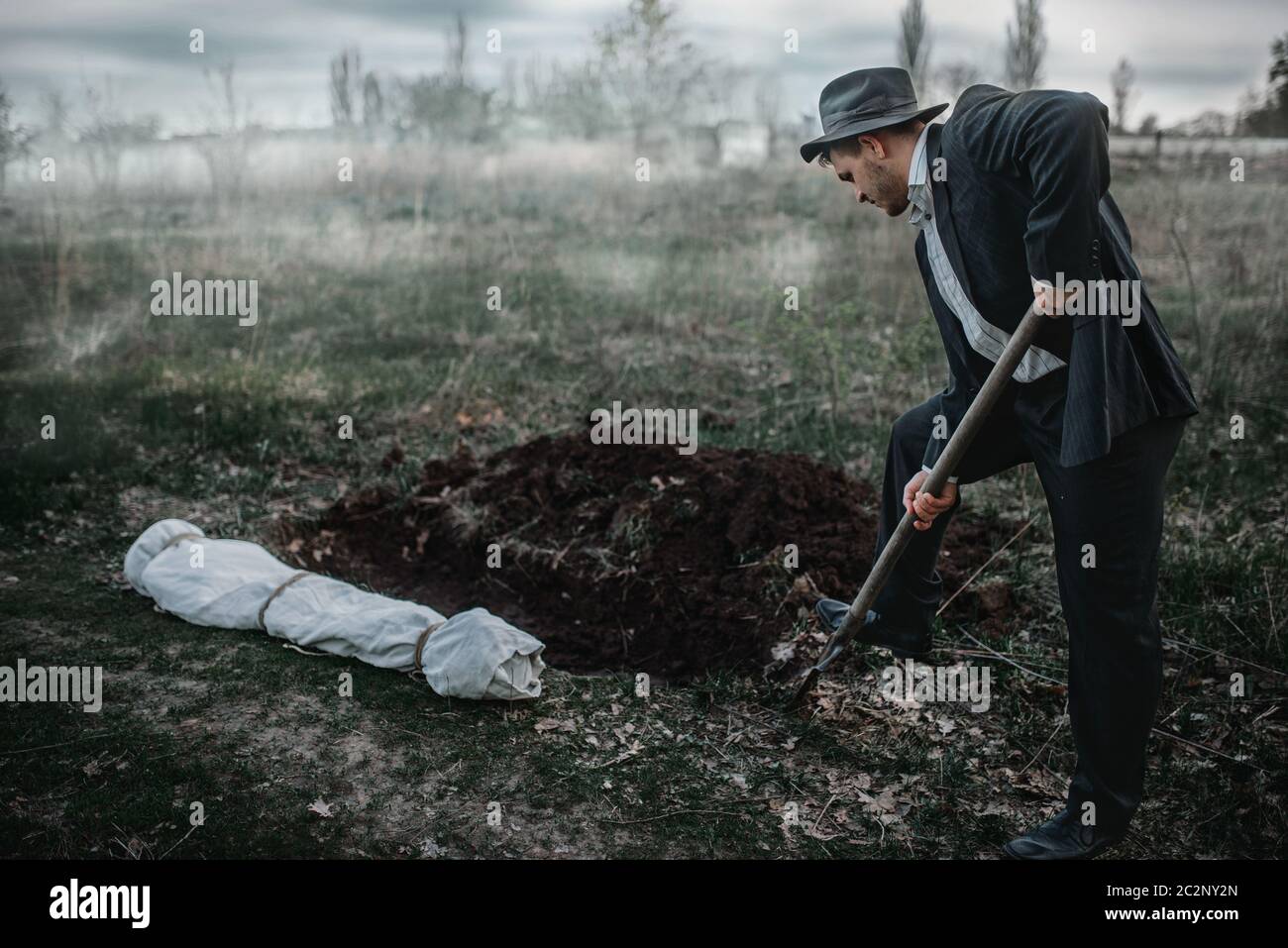 Killer sta scavando una tomba per la vittima nella foresta, il corpo avvolto in una tela, serial maniac concept Foto Stock