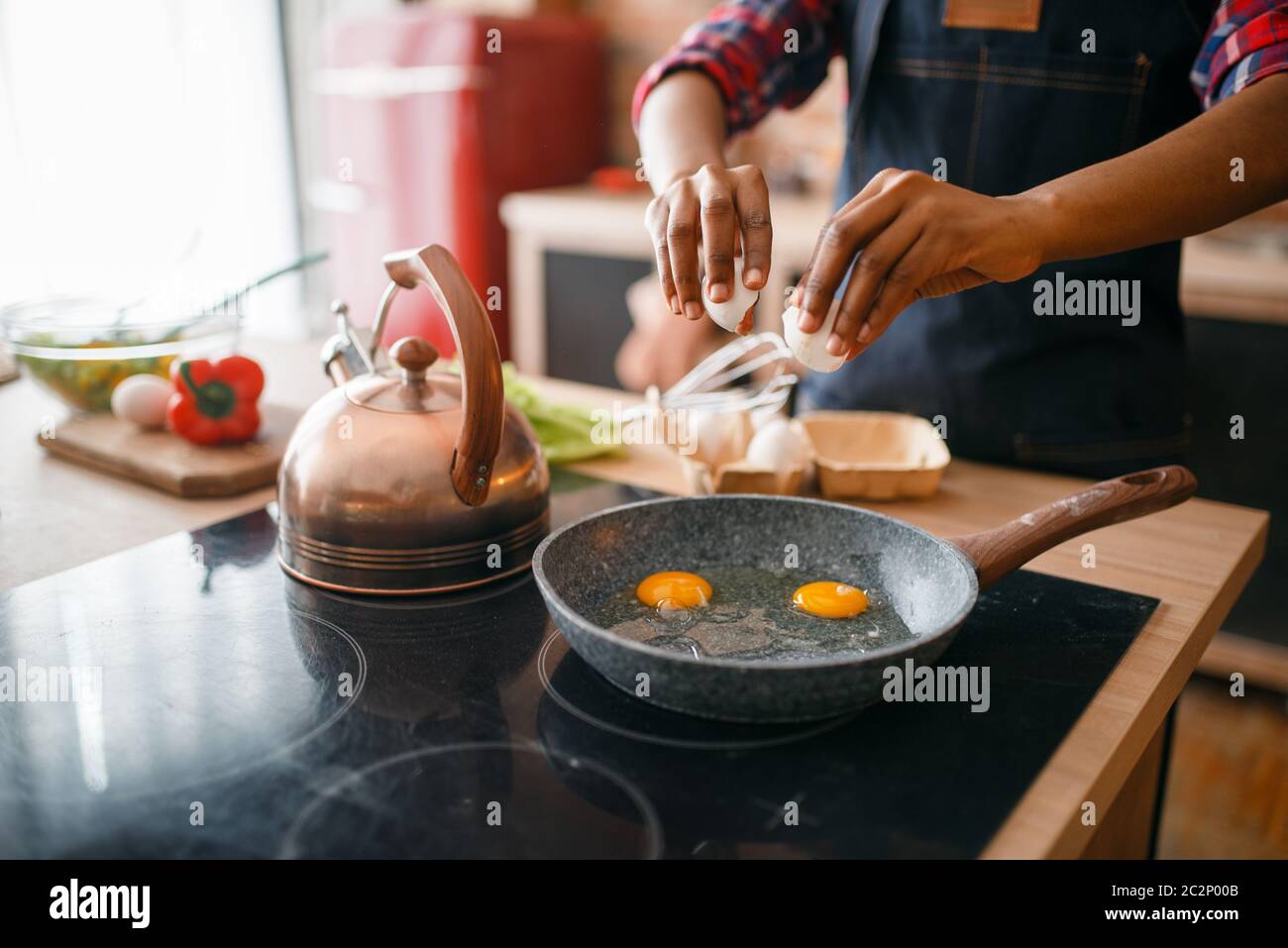 Donna nera che cucinano uova fritte in cucina. Donna africana che prepara la colazione a casa. Stile di vita vegetariano sano Foto Stock