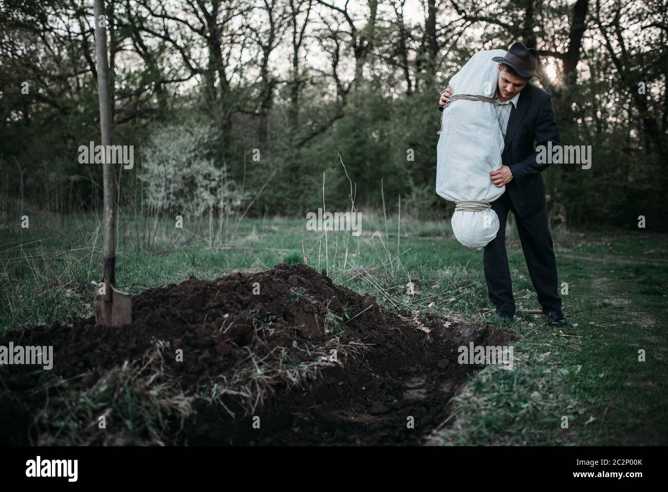 Assassino lancia insanguinata corpo della vittima avvolta in una tela nella tomba, serial maniac concept Foto Stock
