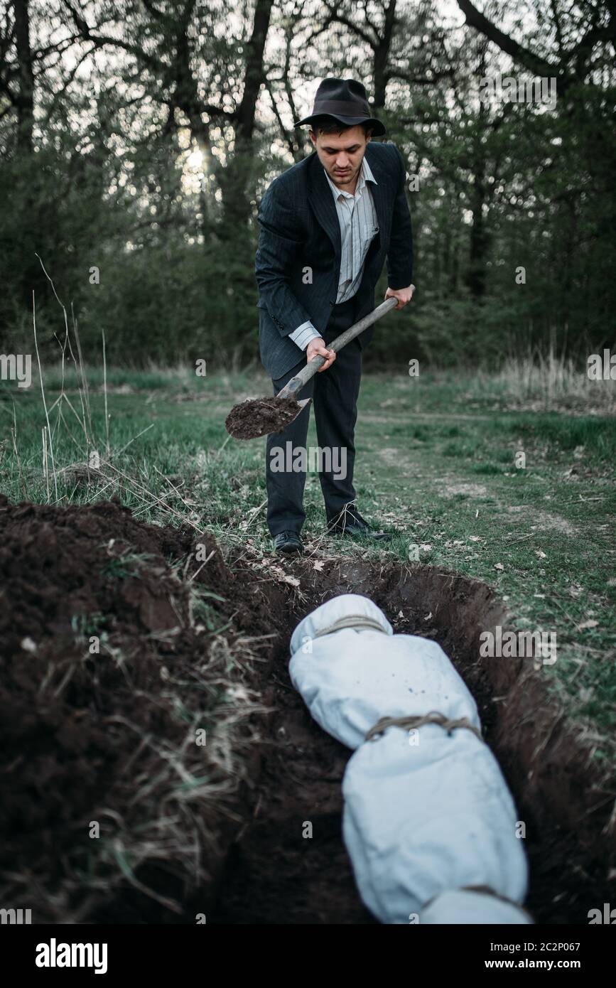 Maniac con una pala seppellisce vittima in un sepolcro il corpo avvolto in una tela, assassino seriale concept Foto Stock