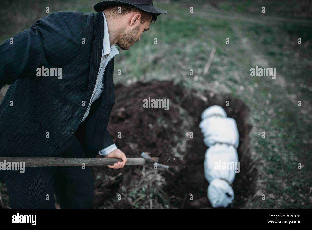 Maniac con una pala seppellisce vittima avvolta in una tela in un sepolcro assassino seriale concetto, criminalità orrore Foto Stock