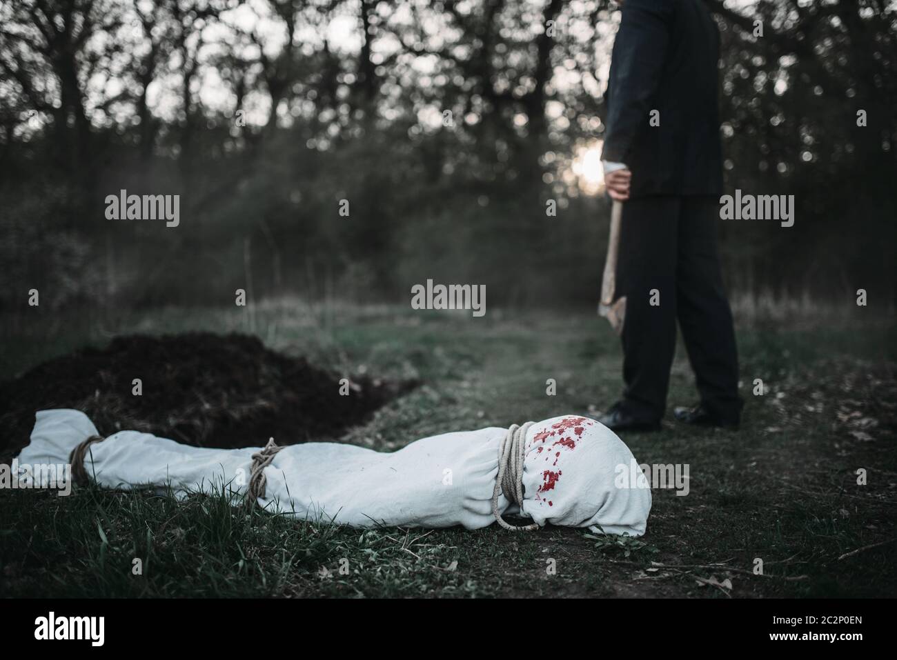 Maniac con un'ascia contro la vittima corpo avvolto in una tela, assassino seriale concept Foto Stock