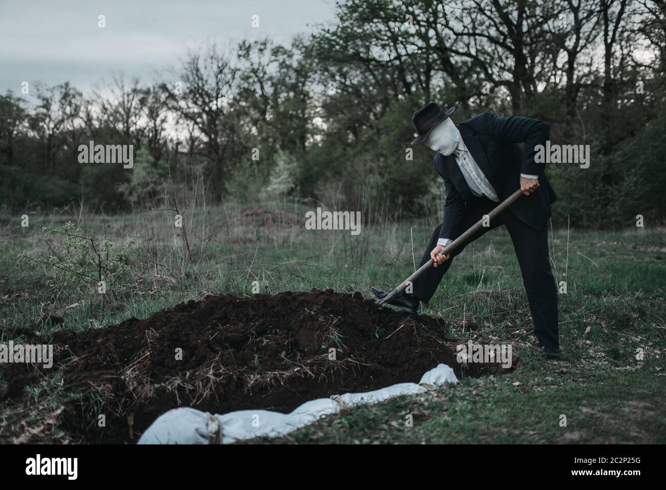 Bloody assassino è scavare una tomba per la vittima nella foresta, il corpo avvolto in una tela, serial maniac concept Foto Stock