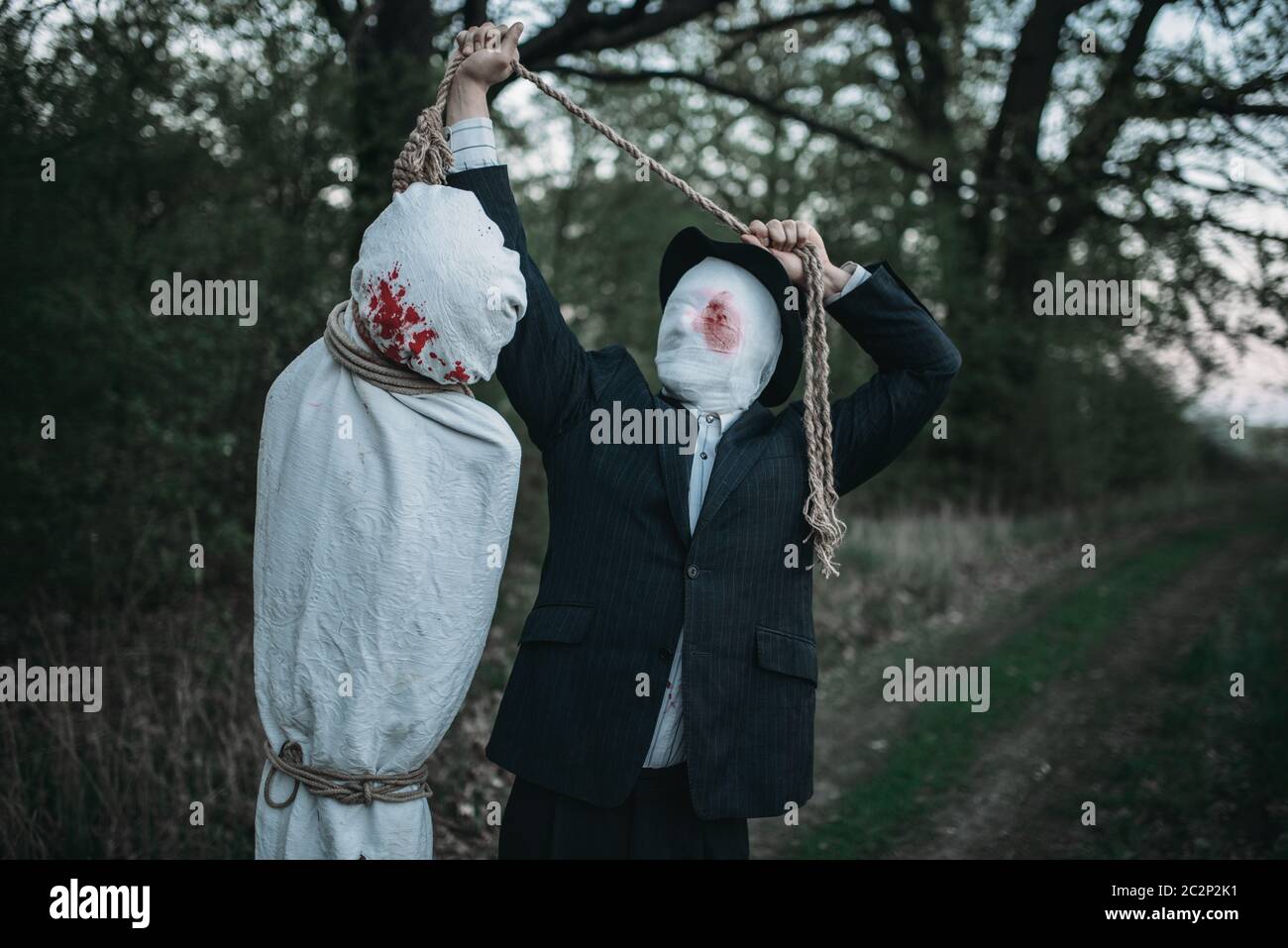 Maniaco seriale si blocca il corpo della vittima avvolta in una tela su un albero, crazy killer concetto, psico assassino Foto Stock