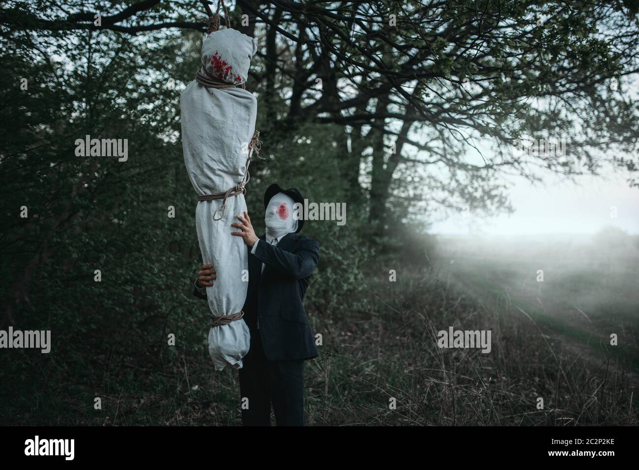 Maniaco seriale si blocca il corpo della vittima avvolta in una tela su un albero, crazy killer concetto, psico assassino Foto Stock