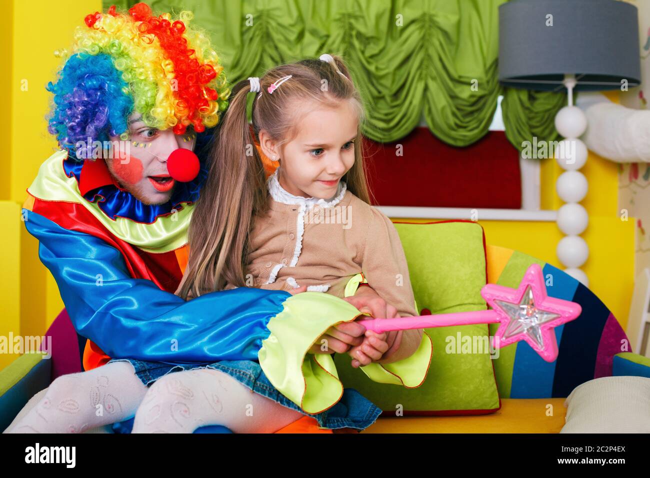 Bambina che gioca con clown allegro in costume divertente. Concetto di amicizia Foto Stock
