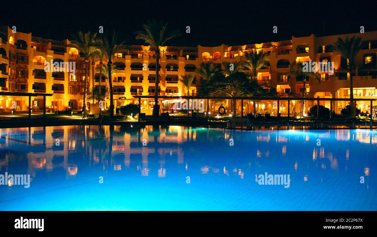 Le luci dell'hotel serale si riflettono nell'acqua della piscina di notte. Luci luminose di un hotel resort ad Hurgh Foto Stock