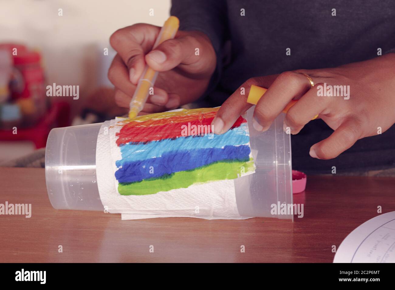 Colorazione di un bambino nero una tazza di plastica riciclata per l'arte e l'artigianato come un modo per far fronte e sostenere la salute mentale durante la quarantena casa covid-19 e blocco Foto Stock