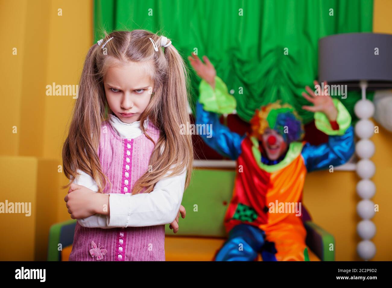 Clown cerca di rallegrare una ragazza triste. Sala giochi sullo sfondo. Foto Stock
