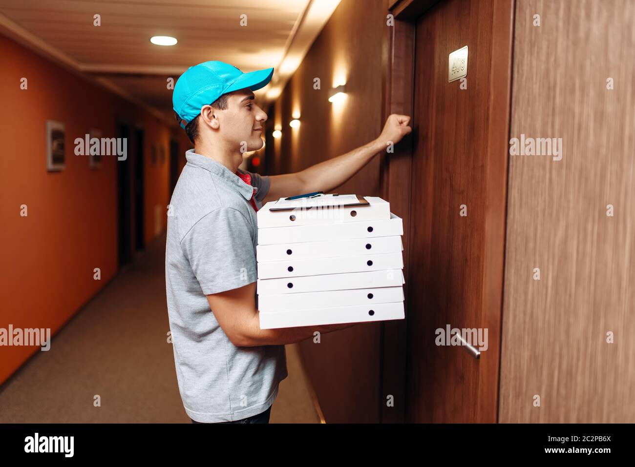 Consegna Pizza ragazzo a bussare alla porta del cliente, servizio di consegna. Corriere dalla pizzeria detiene imballi di cartone interni Foto Stock