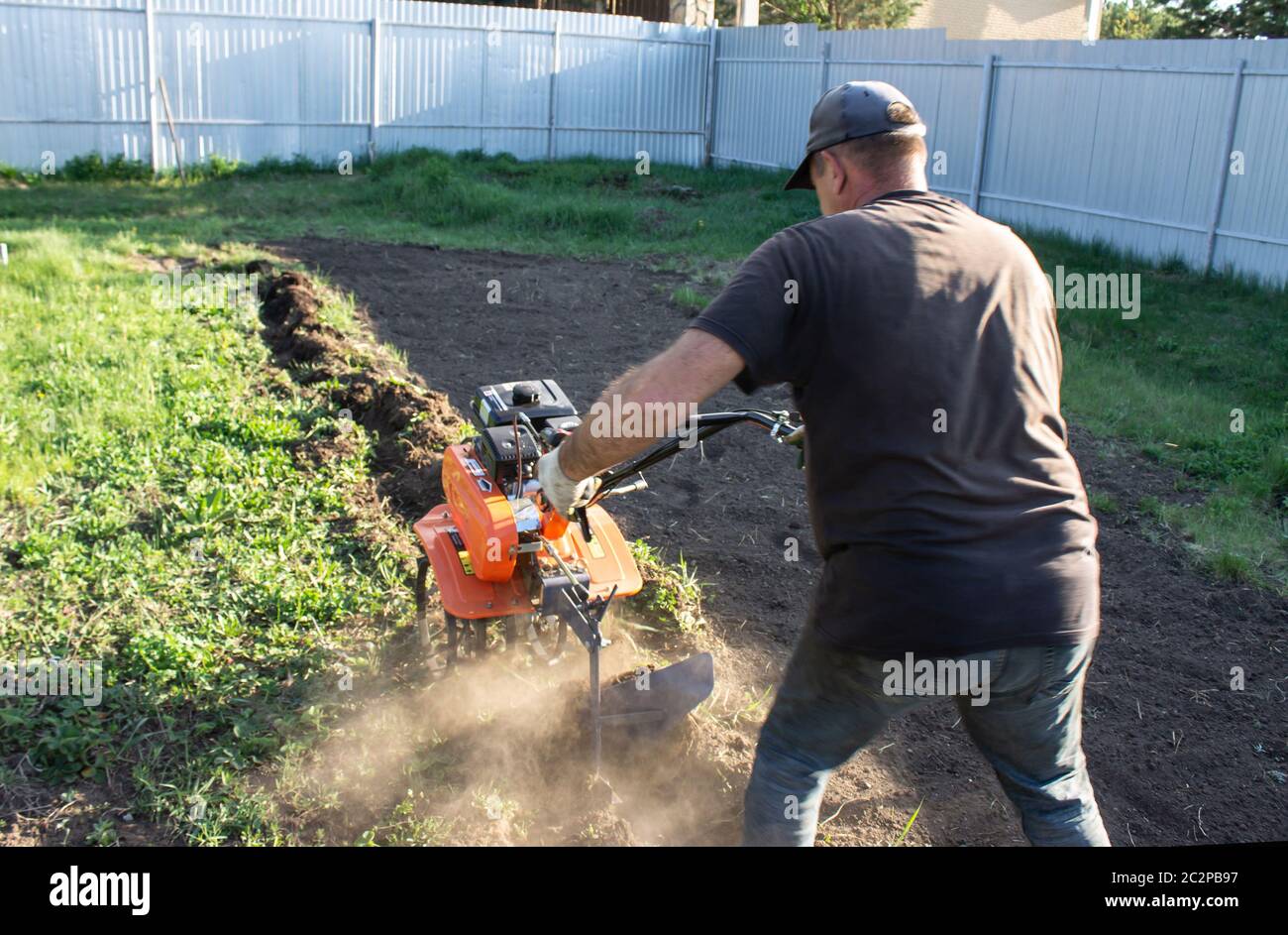 Un uomo che lavora sul campo - sgocciolando il blocco motore con aratro in abiti da lavoro Foto Stock