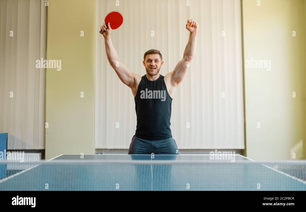 Uomo felice con racchetta ping pong ha alzato le mani in su, torneo interno. Uomo in abbigliamento sportivo, allenamento in ping-pong club Foto Stock