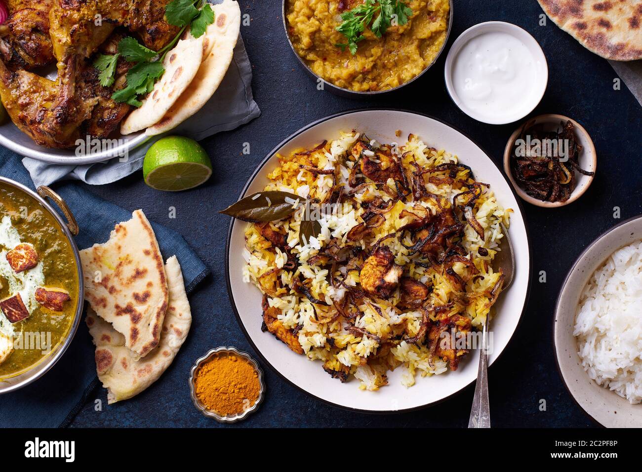 Cena di cucina indiana: Pollo tandoori, biryani, lenticchie rosse con riso naan, paneer di palak e riso basmati su fondo di cemento scuro Foto Stock