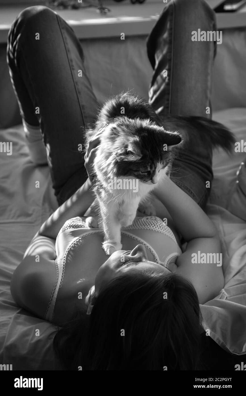 ragazza felice che si steso sul divano e gioca con il suo gatto in luce solare, monocromatico Foto Stock