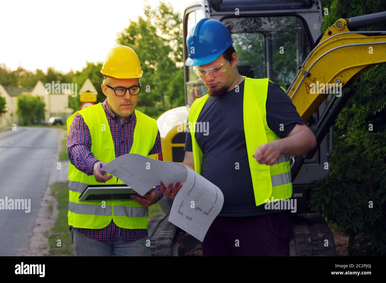 Ingegnere e lavoratore in cantiere con escavatore in background. Un team professionale che lavora nell'edificio delle strade. Due uomini in caschi tal Foto Stock