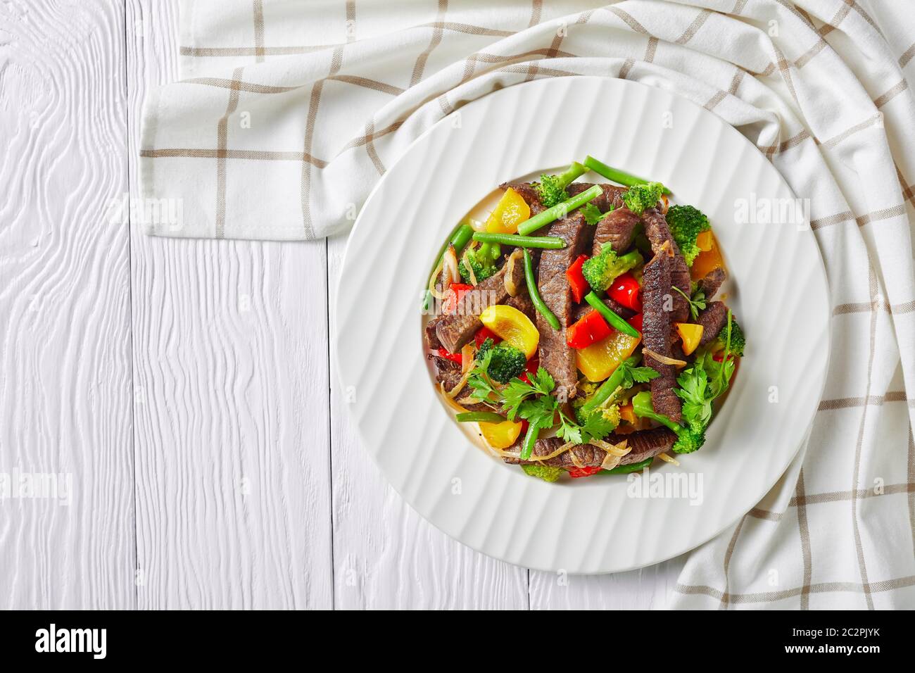 Fajitas di manzo su un piatto bianco con broccoli, fagioli verdi, peperoni dolci gialli e rossi, prezzemolo, cipolla su fondo bianco di legno con piatto da cucina Foto Stock