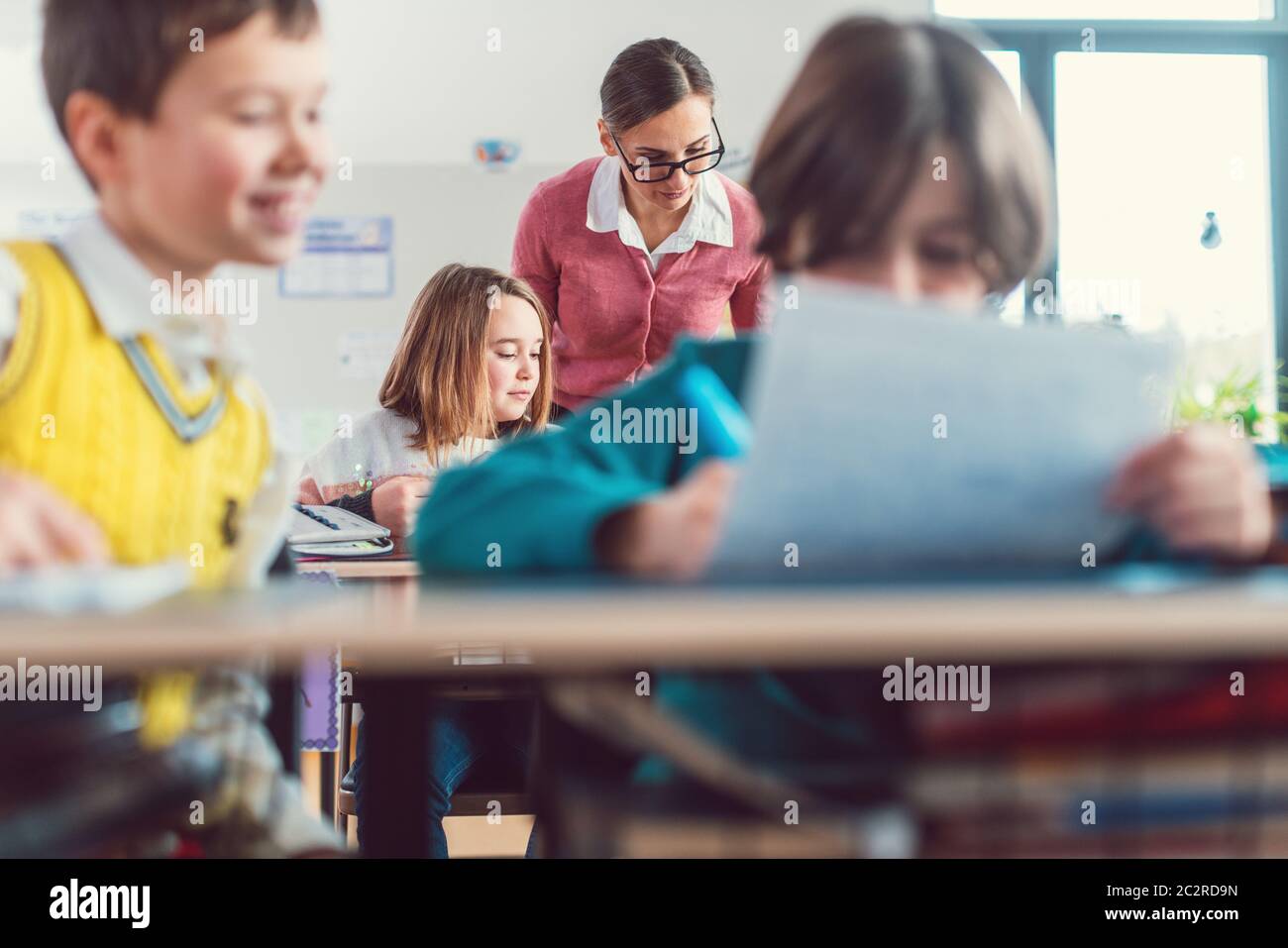 L'insegnante verifica i risultati di un test scritto in classe che va in giro e che parla con gli allievi Foto Stock