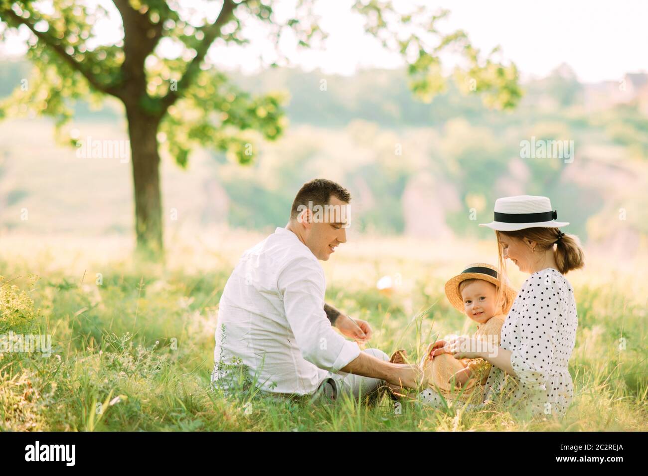 I giovani genitori siedono sull'erba con la figlia mentre camminano nel parco. Foto Stock