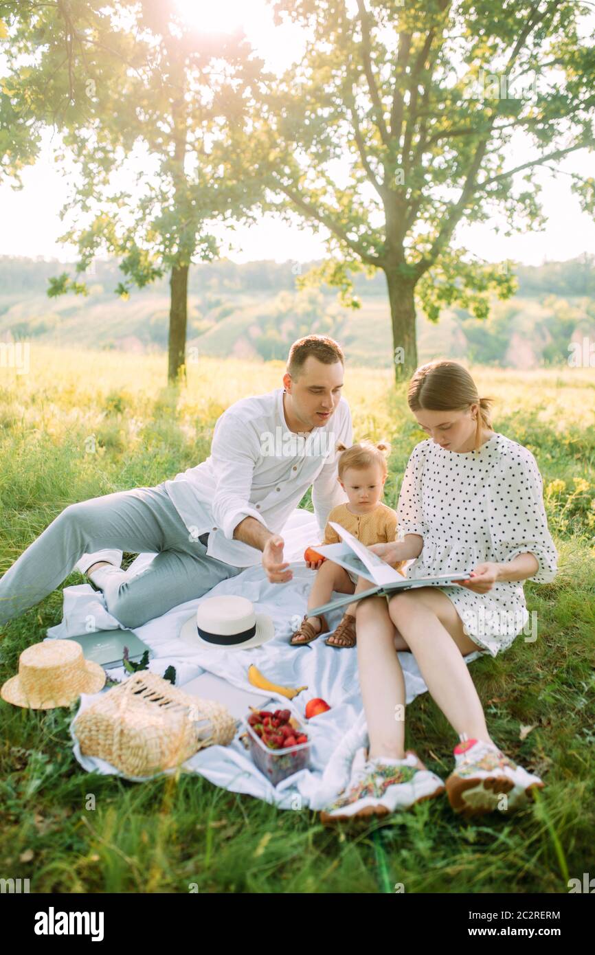 I genitori hanno letto un libro alla loro figlia durante il picnic nel parco. Foto Stock