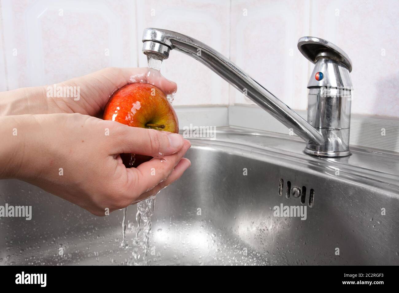 Closeup di mani femminili che lavano la mela sotto l'acqua nel lavandino Foto Stock