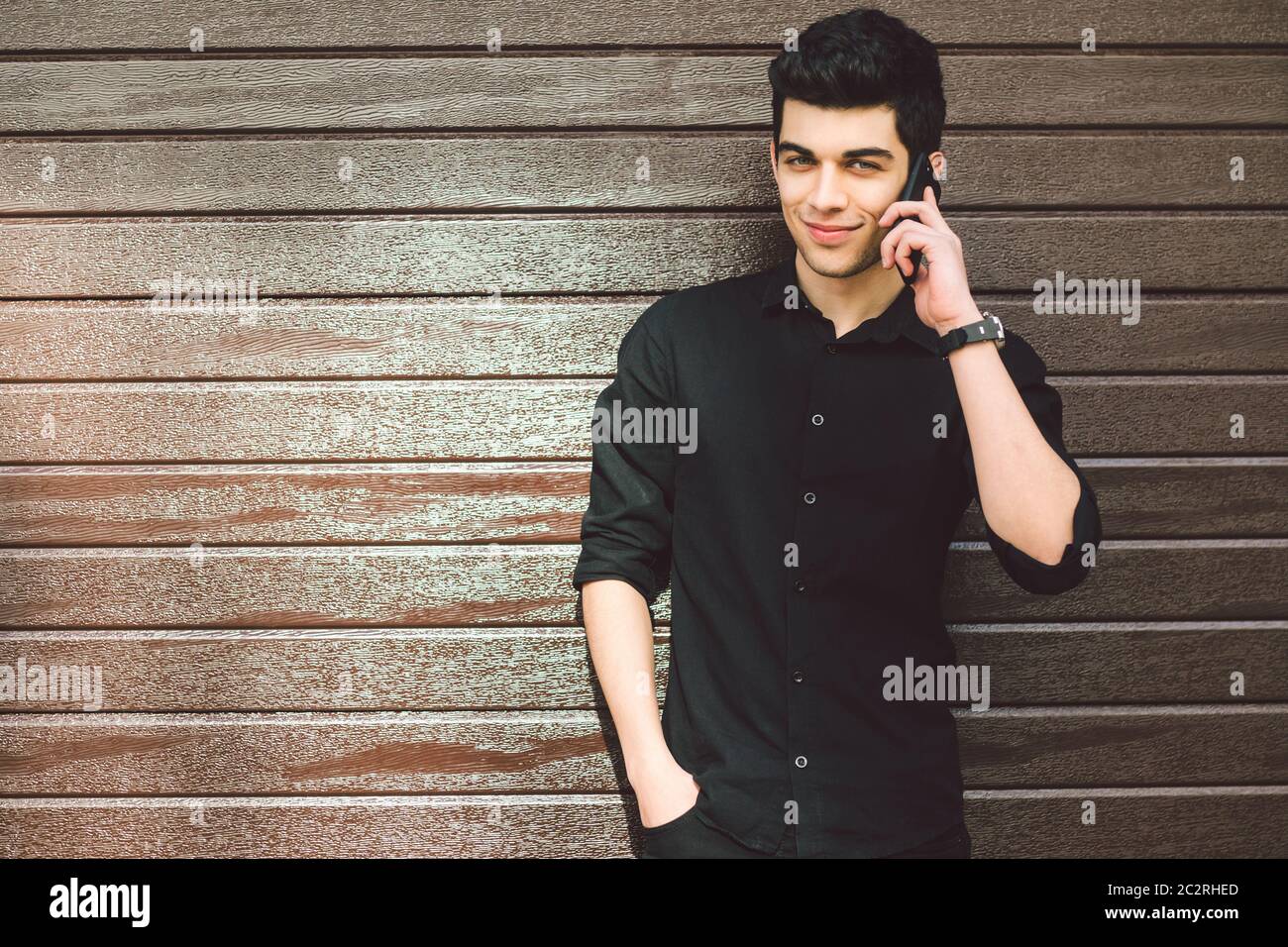 Ritratto modello giovane bel maschio sospetto turco medio orientale brunetta in camicia nera utilizza il telefono a mano per chiamare la tecnologia Foto Stock