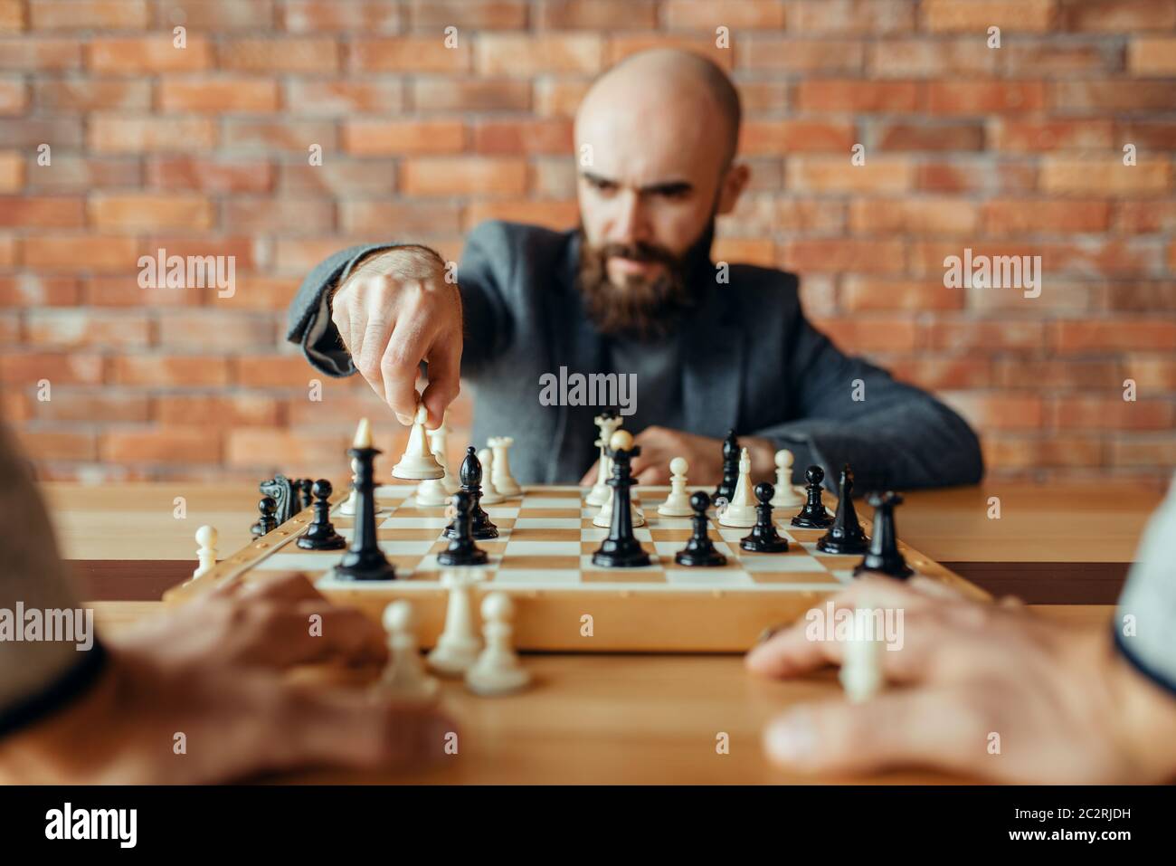Giocatore di scacchi maschile con figura bianca in mano, movimento regina. Chessplayer a bordo, vista frontale, torneo intellettuale al coperto. Scacchiera su tavolo di legno Foto Stock