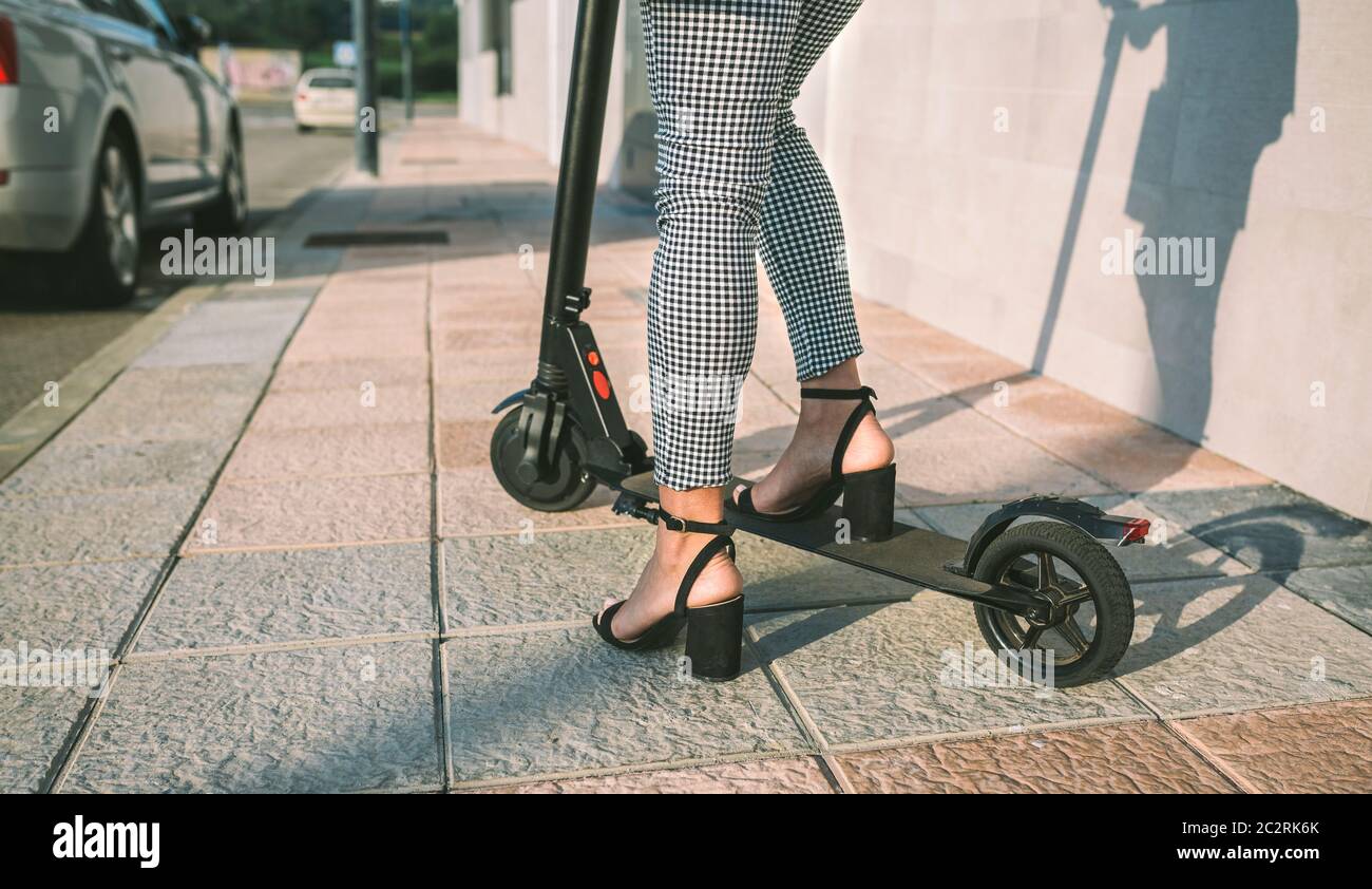 Irriconoscibile imprenditrice gambe con e-scooter all'aperto Foto Stock
