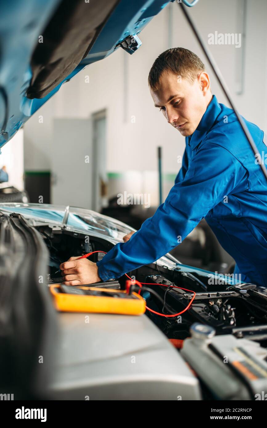 Elettrauto con multimetro controlla il livello di carica della batteria. Auto-service, veicolo diagnosi del cablaggio Foto Stock