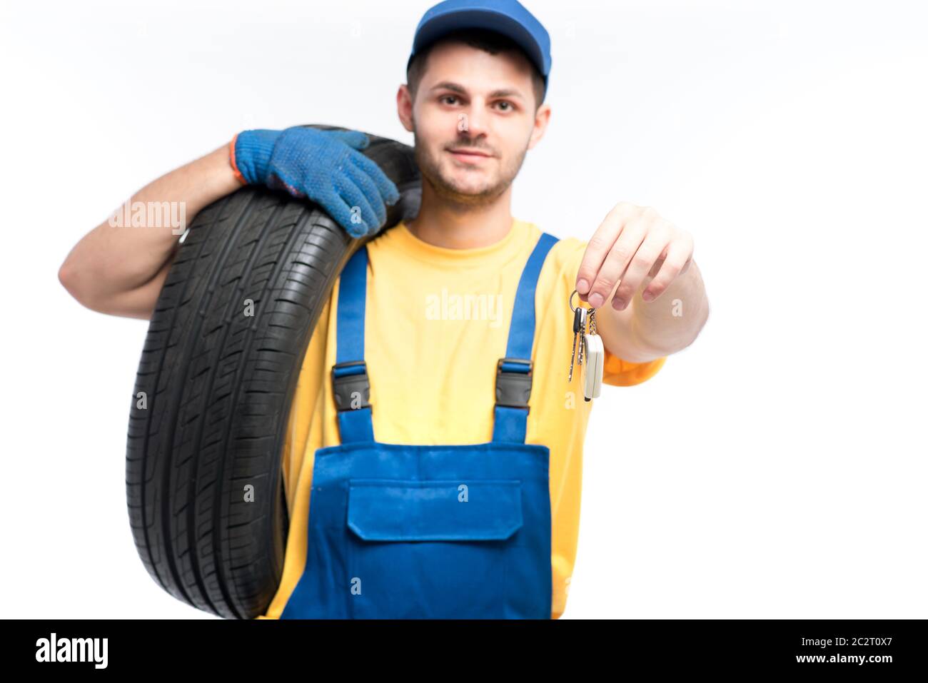 Servizio pneumatici, lavoratore in uniforme blu contiene il pneumatico e la vettura chiavi in mano, sfondo bianco repairman, montaggio ruota Foto Stock