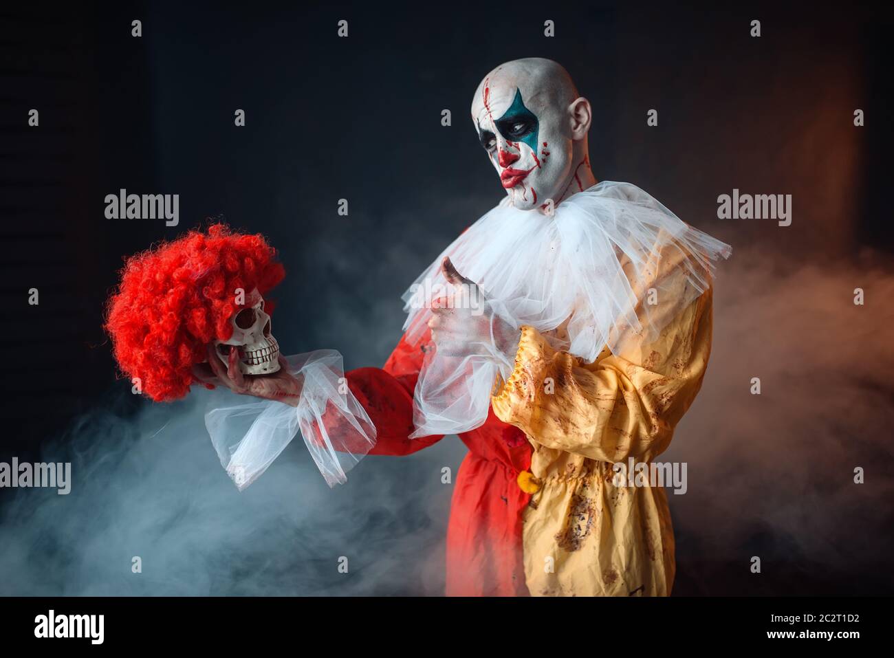 Mad sanguinosa clown detiene il teschio umano in parrucca rosso, horror.  L'uomo con il trucco in costume di carnevale, crazy maniac Foto stock -  Alamy