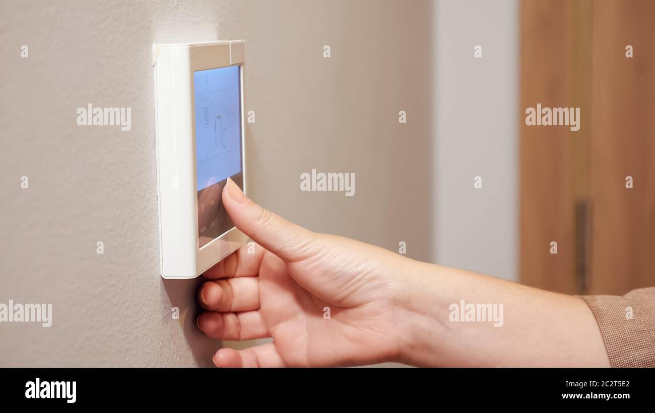 la giovane donna mette a mano il termostato premendo i tasti del pannello di controllo della climatizzazione a parete in un comodo hotel di closeup estremo Foto Stock
