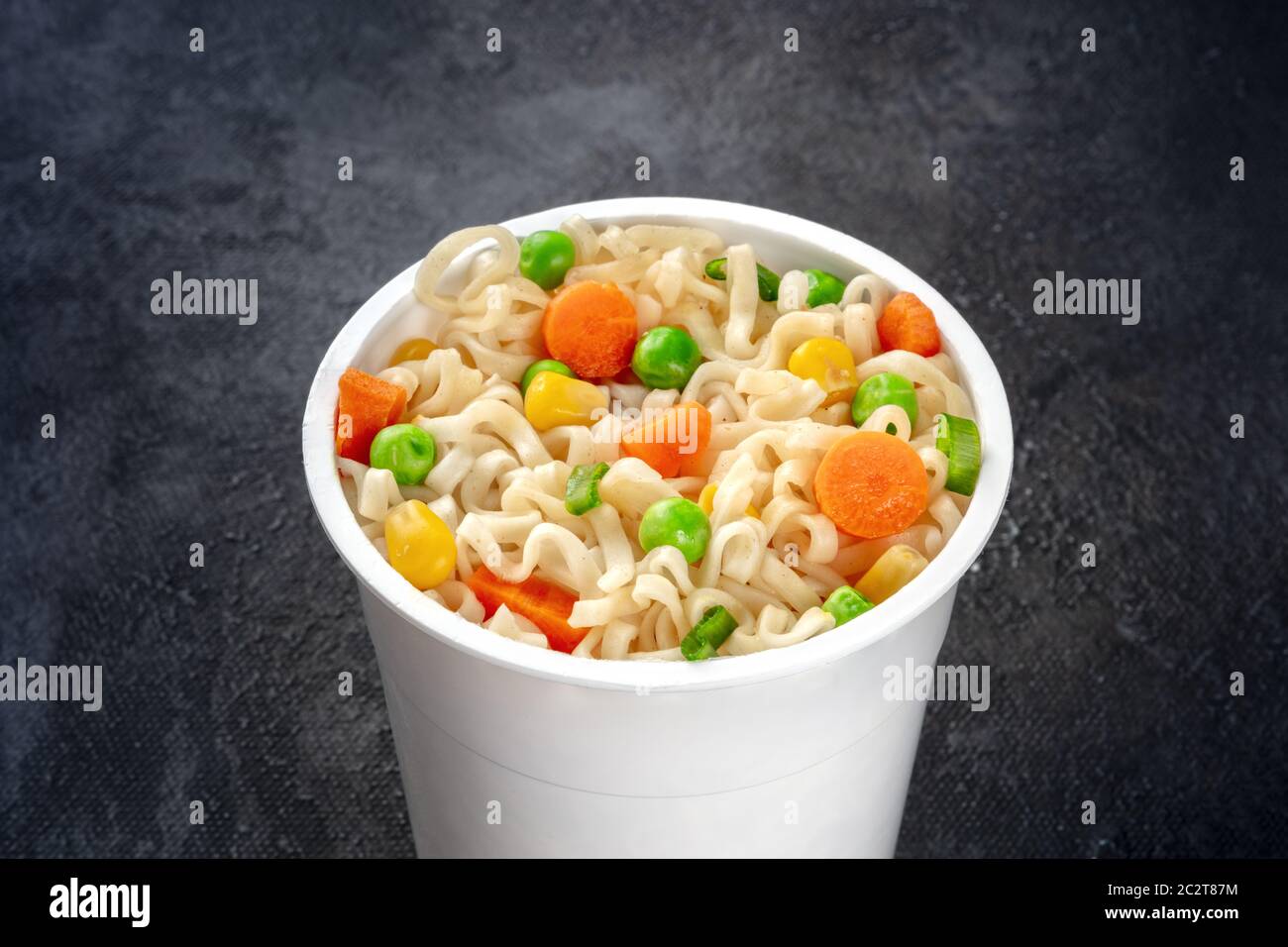 Ramen cup, instant soba noodles in una tazza di plastica con verdure close-up su sfondo nero Foto Stock