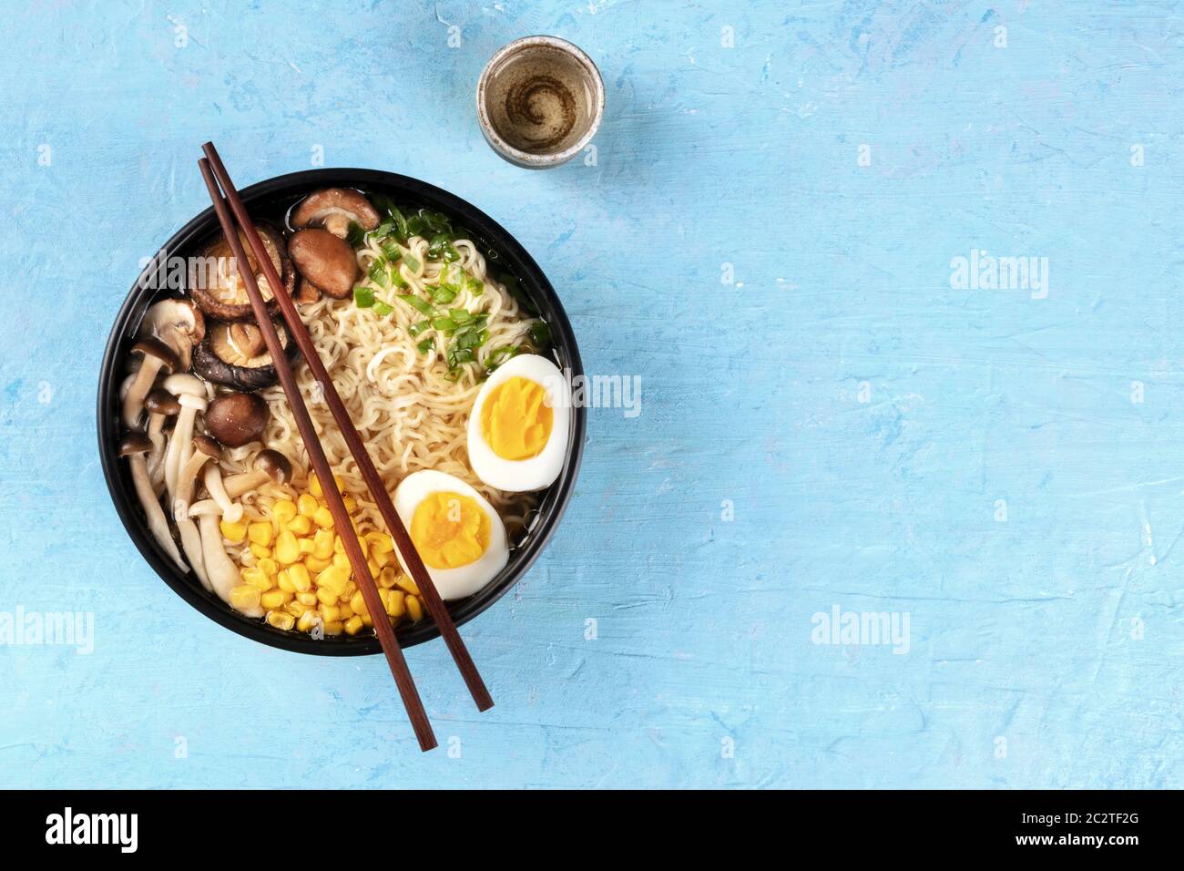 Ramen. Tagliatelle di Soba con uova sode, funghi shiitake e verdure, colpo di testa su sfondo blu con bastoncini, una tazza o Foto Stock
