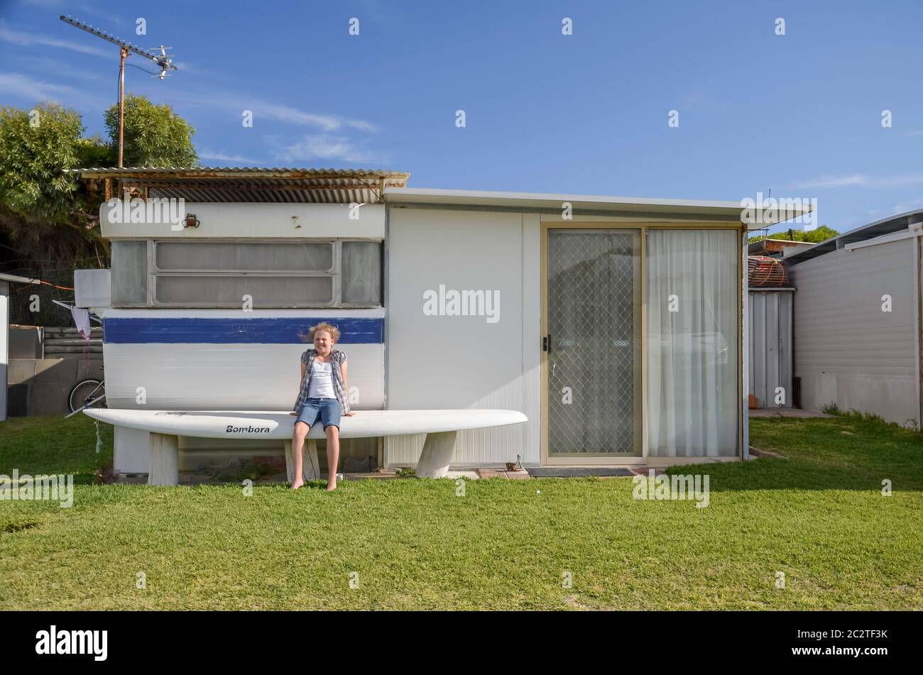 Una delle 4 in una serie, una giovane ragazza si siede di fronte a una casa fatta da una carovana convertita e annesso in un parco caravan a Cervantes, Australia occidentale Foto Stock