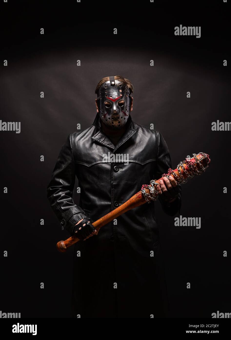 Maniaco sanguinoso in maschera da hockey e cappotto in pelle nera con pipistrello su sfondo nero. Foto Stock