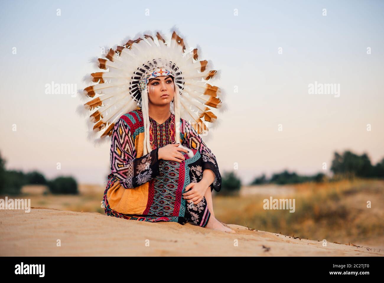 American Indian ragazza in costume nativa in seduta Yoga asana cerimonia rituale. Copricapo fatto di piume di uccelli selvatici. Cherokee, cultura Navajo, Foto Stock