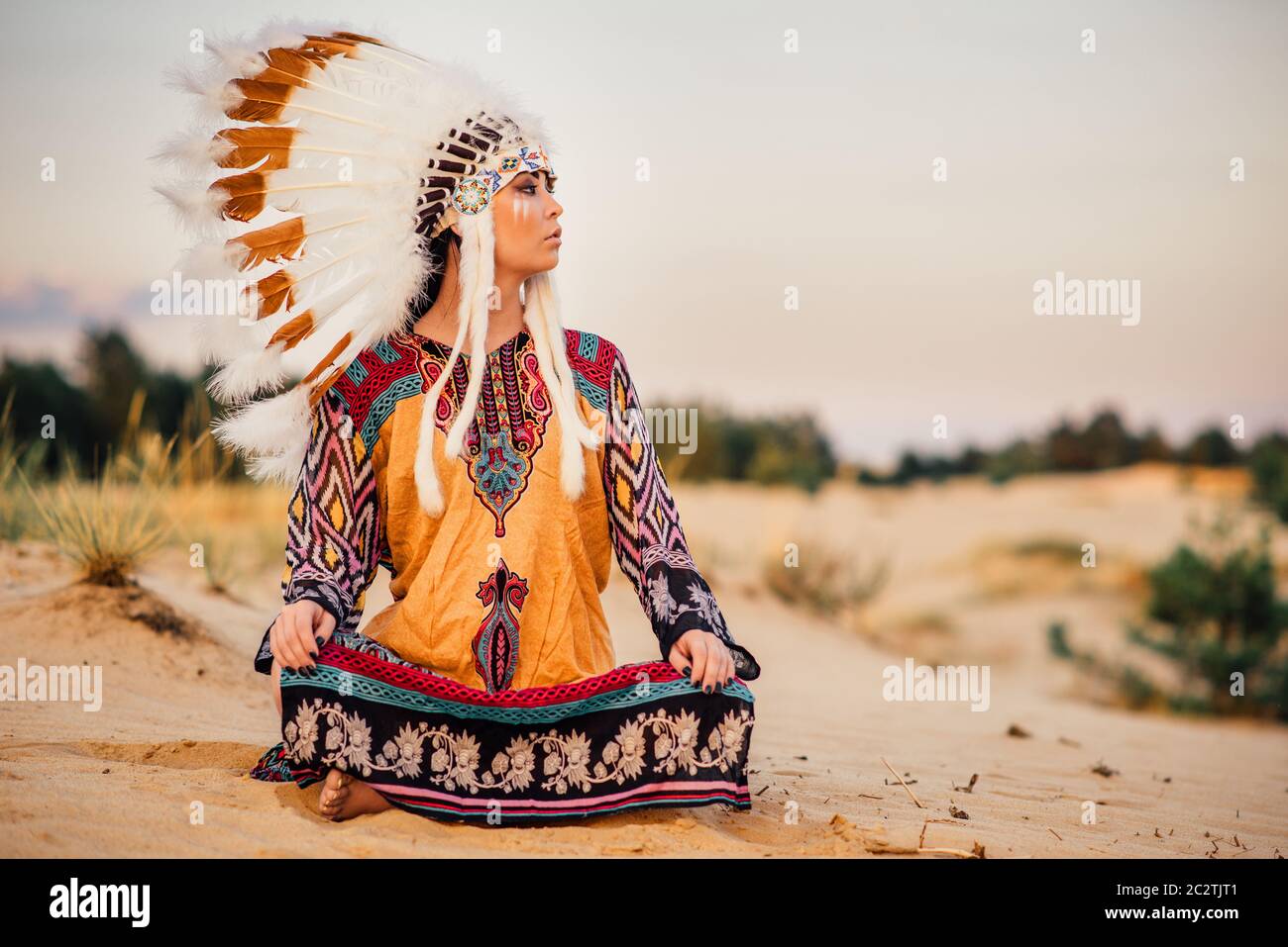 American Indian ragazza in costume nativa in seduta Yoga asana cerimonia rituale. Copricapo fatto di piume di uccelli selvatici. Cherokee, cultura Navajo, Foto Stock