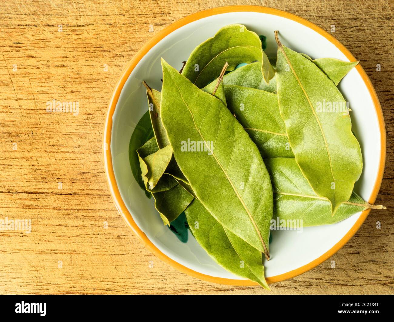 Un piccolo piatto di foglie di alloro essiccate su un tagliere di legno con spazio per la copia Foto Stock