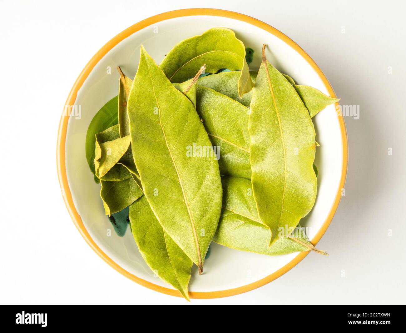 Un piccolo piatto di foglie di alloro essiccato centrato su uno sfondo bianco Foto Stock