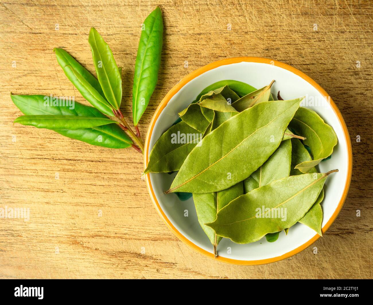 Un piccolo piatto di foglie di alloro secche con un rametto di alloro  fresco su una tagliere di legno Foto stock - Alamy
