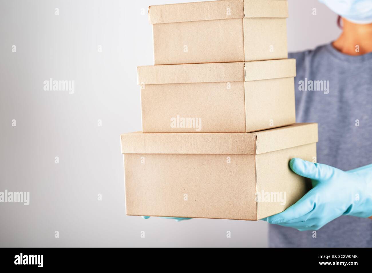 Un addetto al servizio di consegna può contenere una scatola con guanti e una maschera per proteggerla da virus e malattie su sfondo bianco. Foto Stock