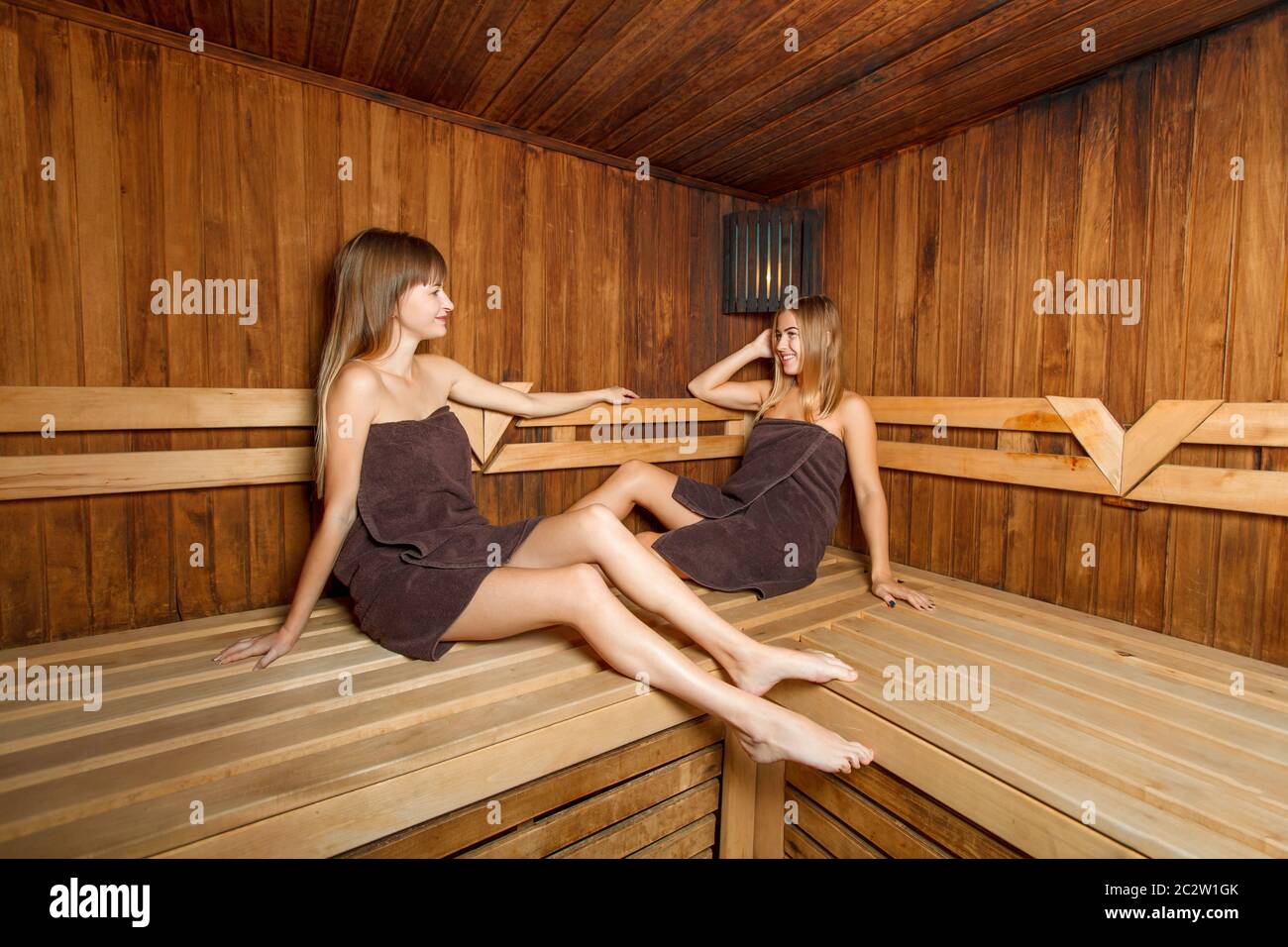 Due belle donne ridenti seduti sulla panchina e che parlano in sauna. Wellnes. Foto Stock