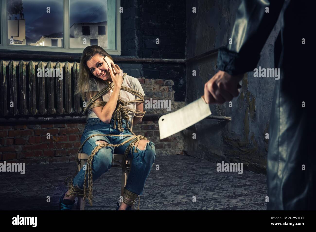 Vittima femmina del maniac legato ad una sedia e tenta di chiamare per la guida tramite telefono. Assassino mano con carne cleaver Foto Stock