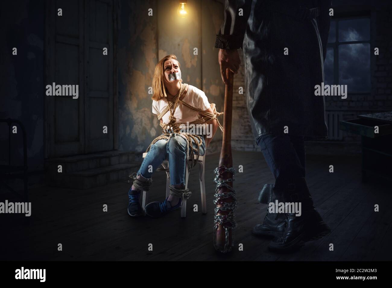 Maniaco seriale con la mazza da baseball in piedi contro la femmina vittima legata con funi ad una sedia. Crazy butcher caccia Foto Stock