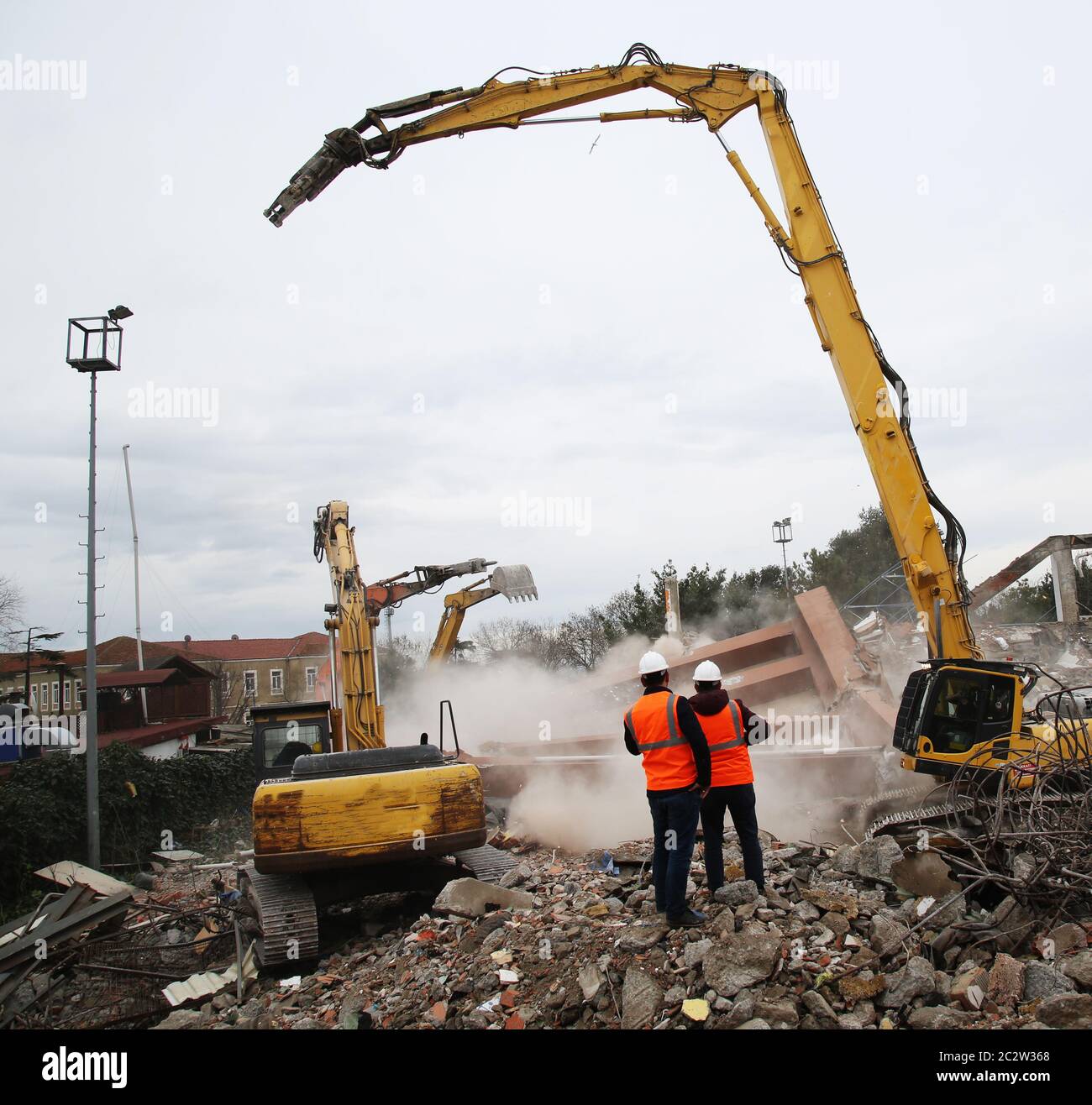 Ingegnere mans in casco e giacca che controlla cantiere esterno. Uomo tecnico che guarda i macchinari sul sito di demolizione. Foto Stock