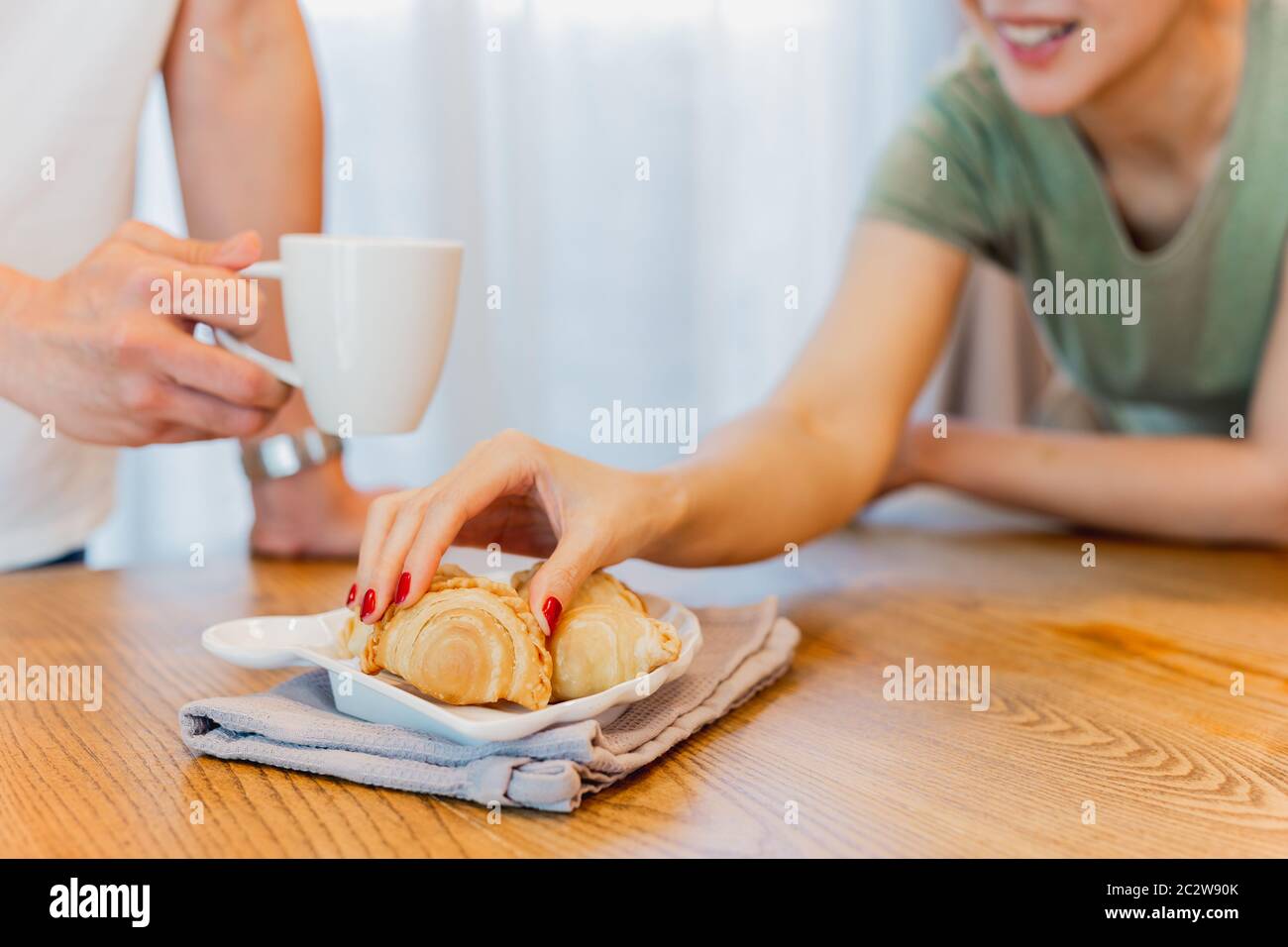 Donne mano che prende gli spuntini del puff del curry con l'amico che tiene una tazza di caffè a casa. Foto Stock