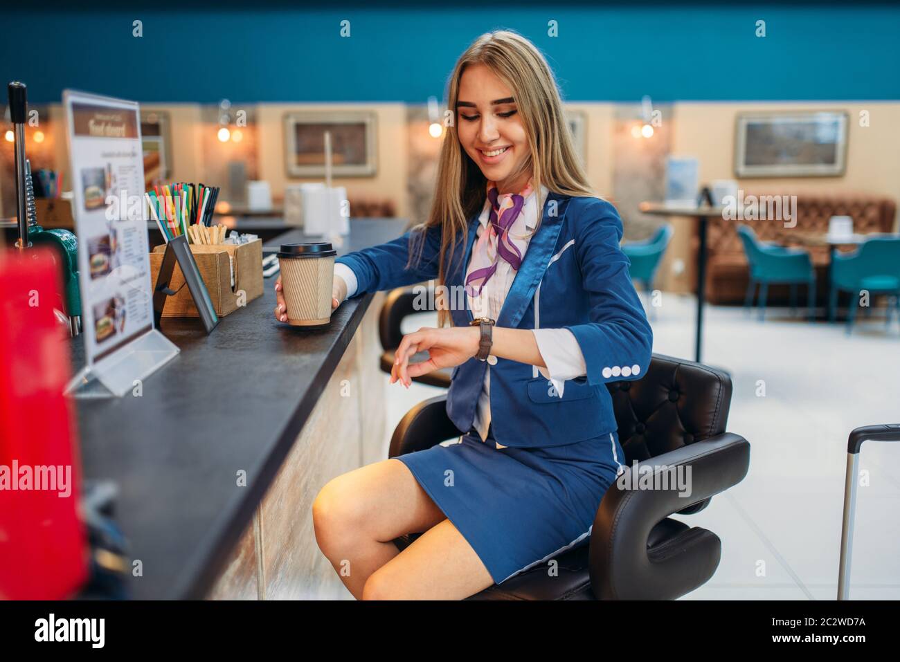 Hostess con il bagaglio a mano beve caffè in aeroporto cafe. Hostess con il bagaglio e assistente di volo con il bagaglio a mano, aviatransportations job Foto Stock