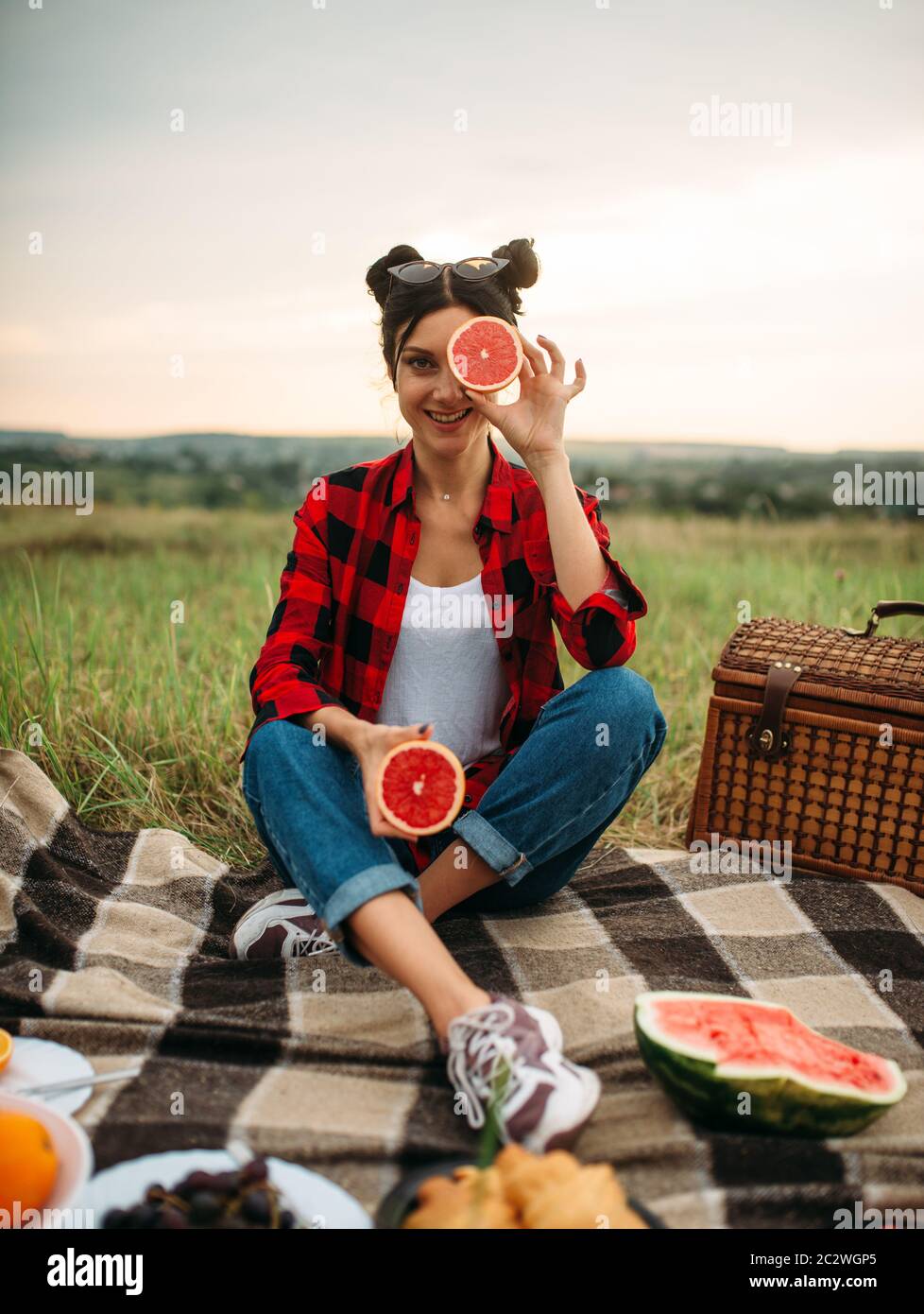 Giovane donna seduta su plaid, picnic nel campo estivo. Giuncata romantici, vacanze felici Foto Stock