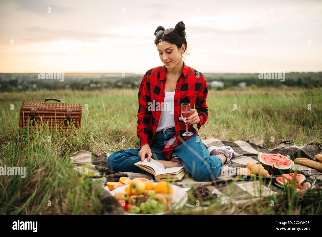 Carino donna con bicchiere di vino legge prenota, picnic sul prato. Giuncata romantici, vacanze felici Foto Stock