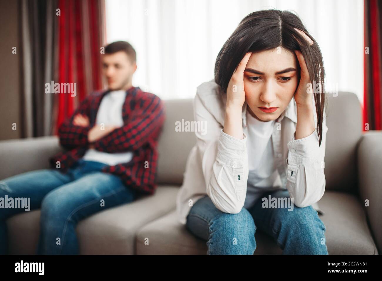 Ha sottolineato la moglie seduta sul lettino, triste marito sullo sfondo, conflitto familiare. Uomo infelice e la donna a litigare Foto Stock